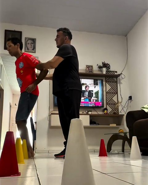 O Nilberto acompanhando o aluno num exercício entre cones, dentro de casa.
