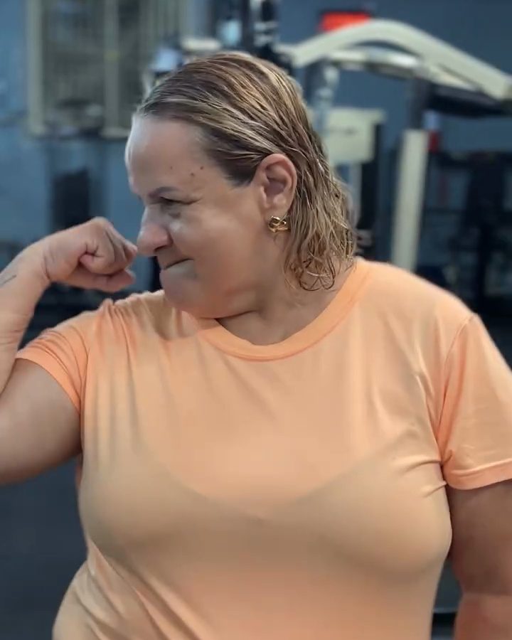 Dona Sheila na academia, mostrando o braço forte com um sorriso.